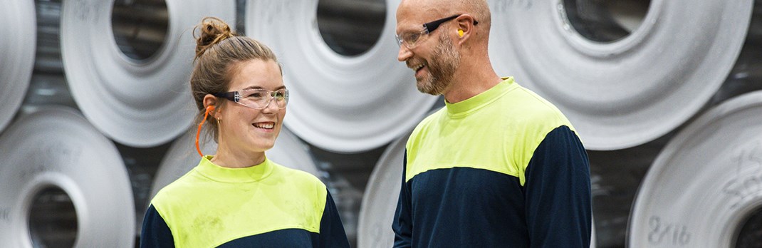 Two employees smiling in front of aluminium coils.