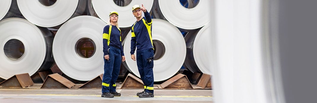 Two employees in front of a stack of aluminium coils.