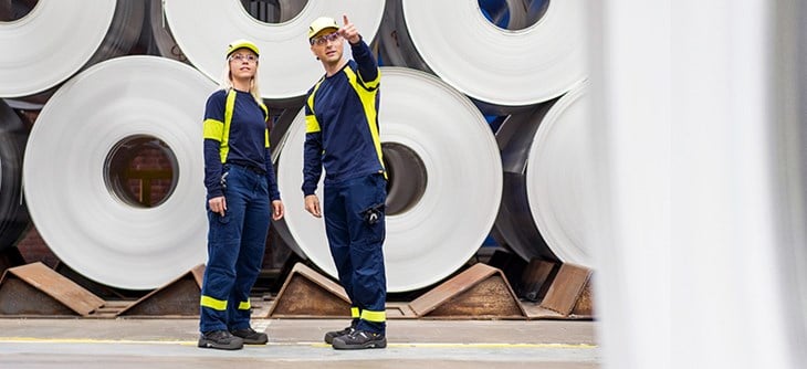 Two employees in front of a stack of aluminium coils.