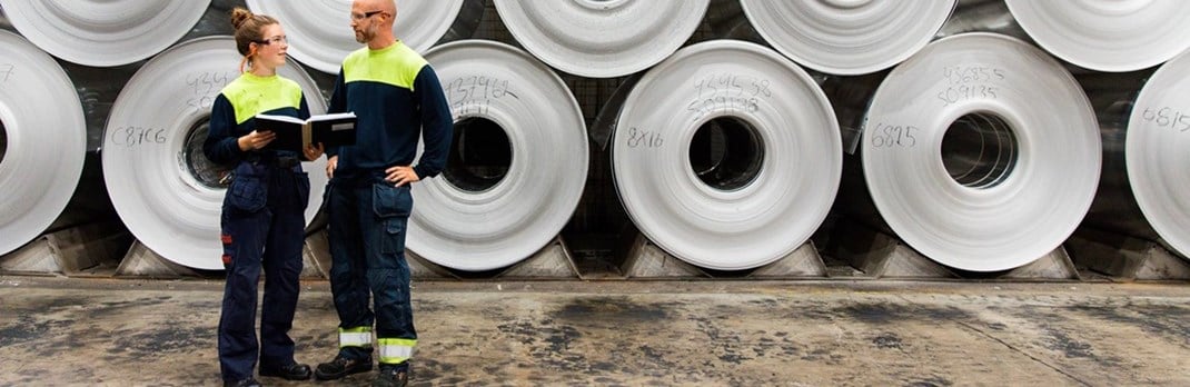 Two employees in front of stacked aluminium coils.
