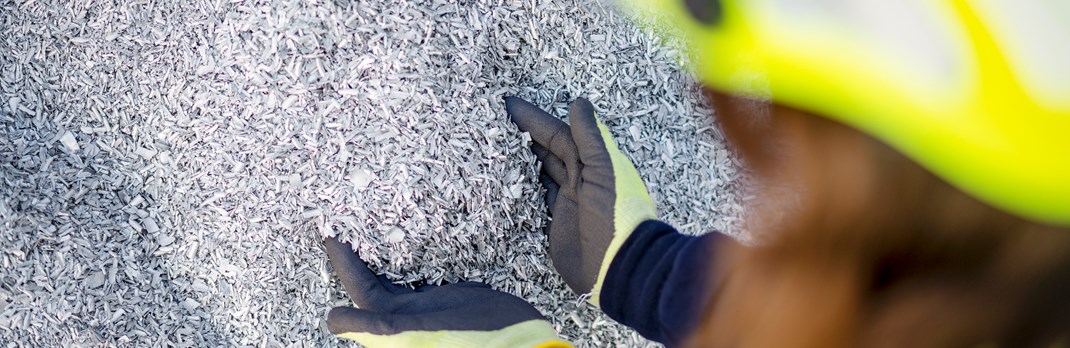 Two hands reaching into an assortment of small pieces of aluminium scrap.